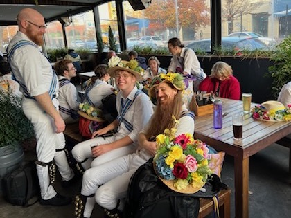 Limestone Morris lounging around in their lovely kit outside at Bentspoke. Flowery hats are seen resting on the table, and various dancers are alternately smiling at the camera and deep in conversation with each other.